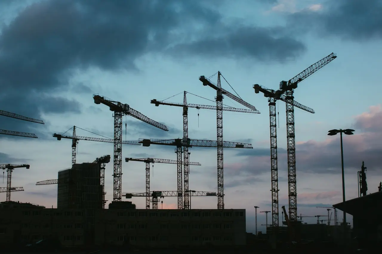Grues de chantier en silhouette sous un ciel nuageux au crépuscule